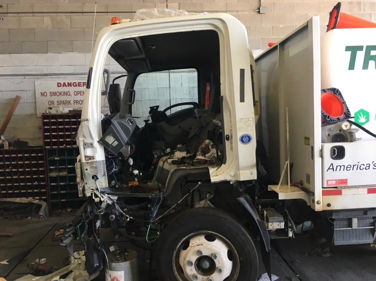A wrecked white cab-over box truck in the Astro Collision shop, the front of the cab torn away and its wiring and dashboard exposed