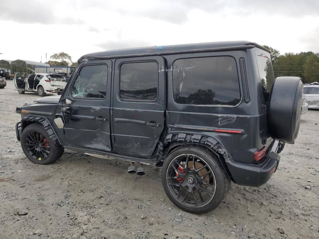 Black Mercedes G-Class with dented doors, scraped side panels and a shattered driver window after a side impact