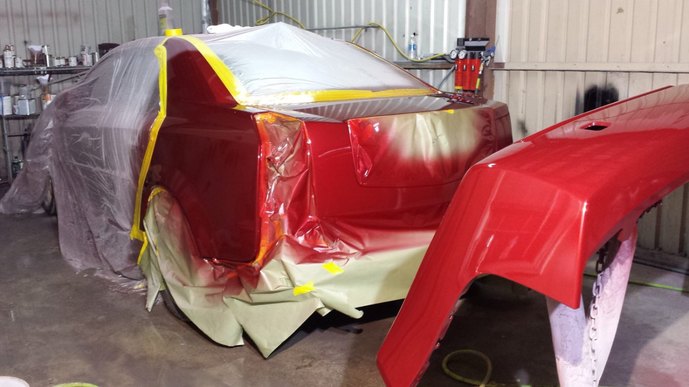Red car masked off in the paint booth for a two-tone respray, with its matching freshly painted red bumper cover — Astro Collision Houston
