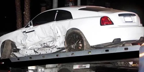 White luxury coupe with a crushed driver side, loaded on a flatbed tow truck at night