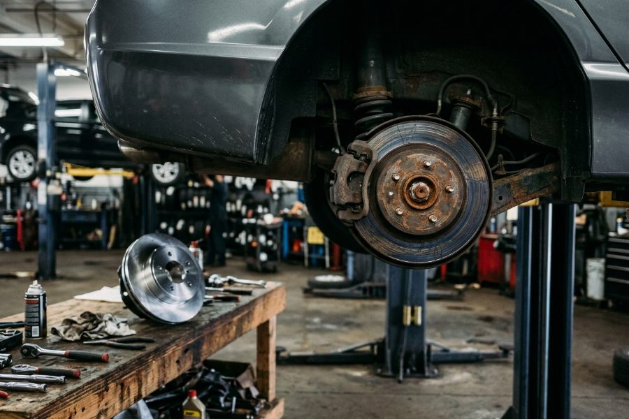 Worn, rusted brake rotor on a lifted car with a new replacement rotor on the workbench